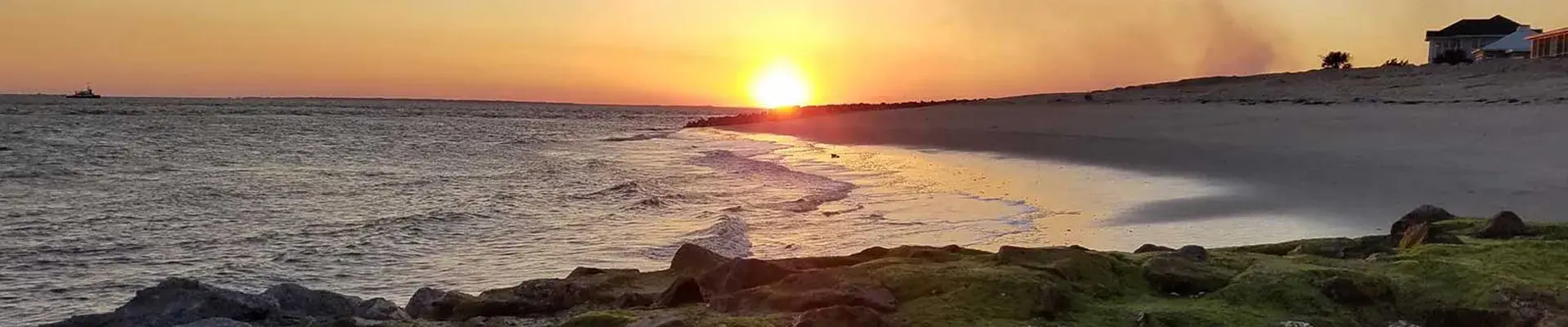 Golden sunset reflecting over ocean waves along a sandy beach with moss-covered rocks