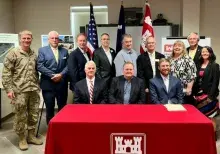 Group photo of military and civilian officials at a U.S. Army Corps of Engineers coastal storm risk management project signing event, with a red table featuring the Corps of Engineers castle emblem in the foreground.